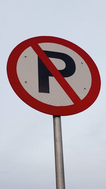 Close-up view of a circular no-parking sign mounted on a metal pole against a cloudy sky. The sign features a bold black letter 'P' with a red diagonal line crossing it out, indicating parking restrictions. The sign is situated near a property entrance or loading zone, which may be relevant for home relocation, furniture transport, or moving services such as those provided by Dulwich Removals. This parking suspension is significant for planning efficient clearance during house removals, ensuring vehicles and moving trucks have access to the premises without obstruction. The sign is clearly visible, with a clean surface and vibrant colors, supporting the coordination of the loading process and move planning, especially where parking regulations impact logistics for domestic or commercial relocations near East Dulwich station or similar locations.
